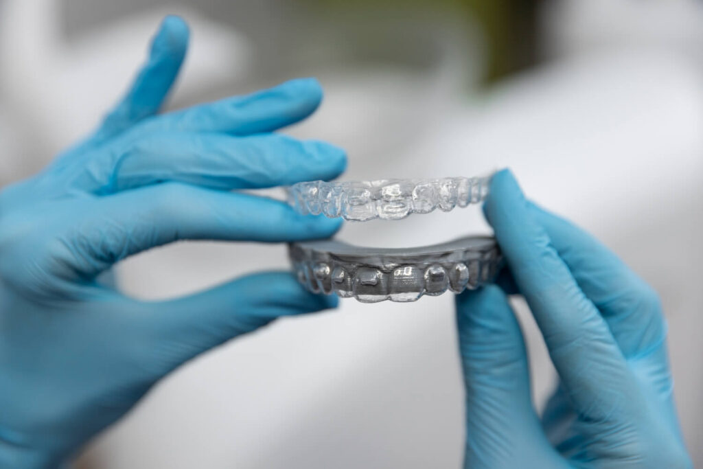 Dentista com luvas azuis segura alinhadores invisíveis transparentes, mostrando a tecnologia e previsibilidade do tratamento em Brasília.