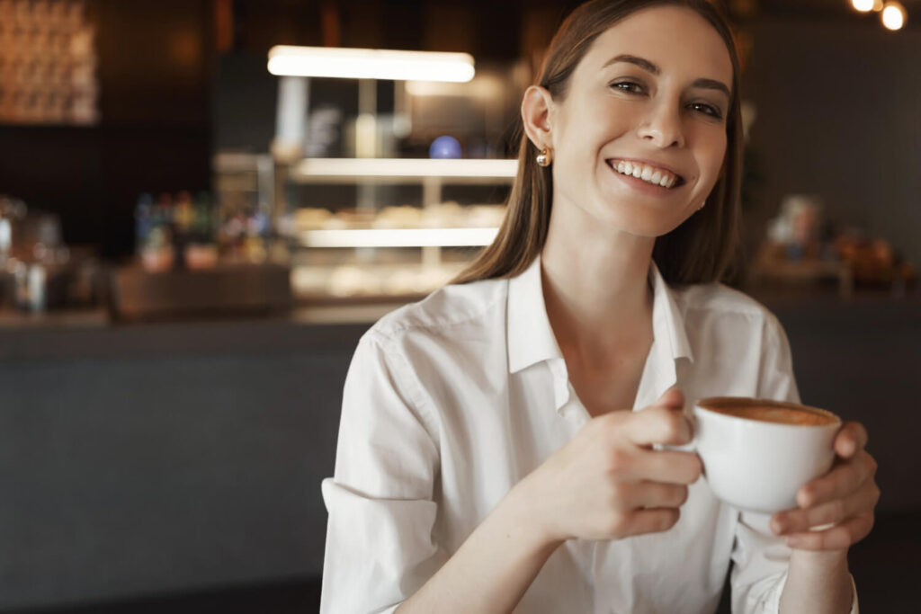 Mulher com sorriso alinhado e branco segura xícara de café em cafeteria, ilustrando cuidados da dieta pós-clareamento dental em Brasília.