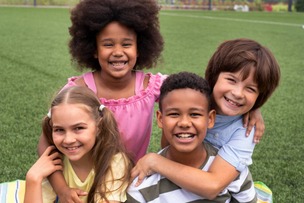 Quatro crianças felizes sorrindo juntas em um gramado em Brasília, exibindo sorrisos e dentes, ideal para ortodontia preventiva.