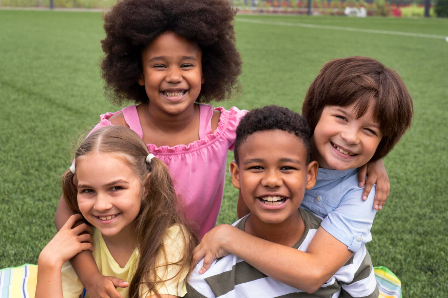 Quatro crianças felizes sorrindo juntas em um gramado em Brasília, exibindo sorrisos e dentes, ideal para ortodontia preventiva.