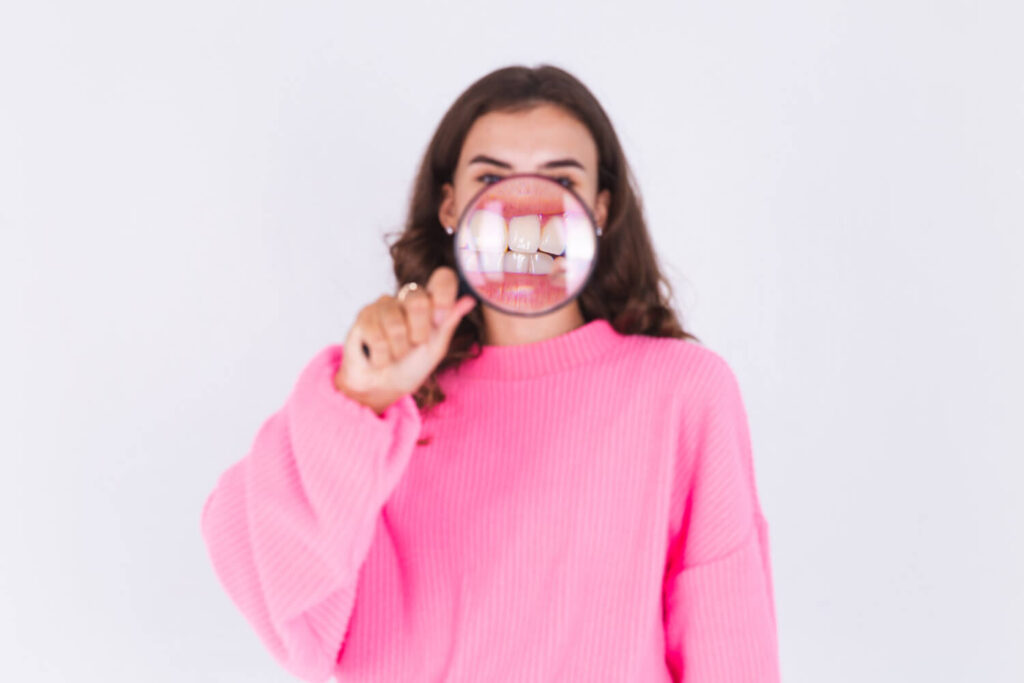 Mulher com blusa rosa segura uma lupa que amplia seus dentes, mostrando detalhes da gengiva para tratar a retração gengival em Brasília.